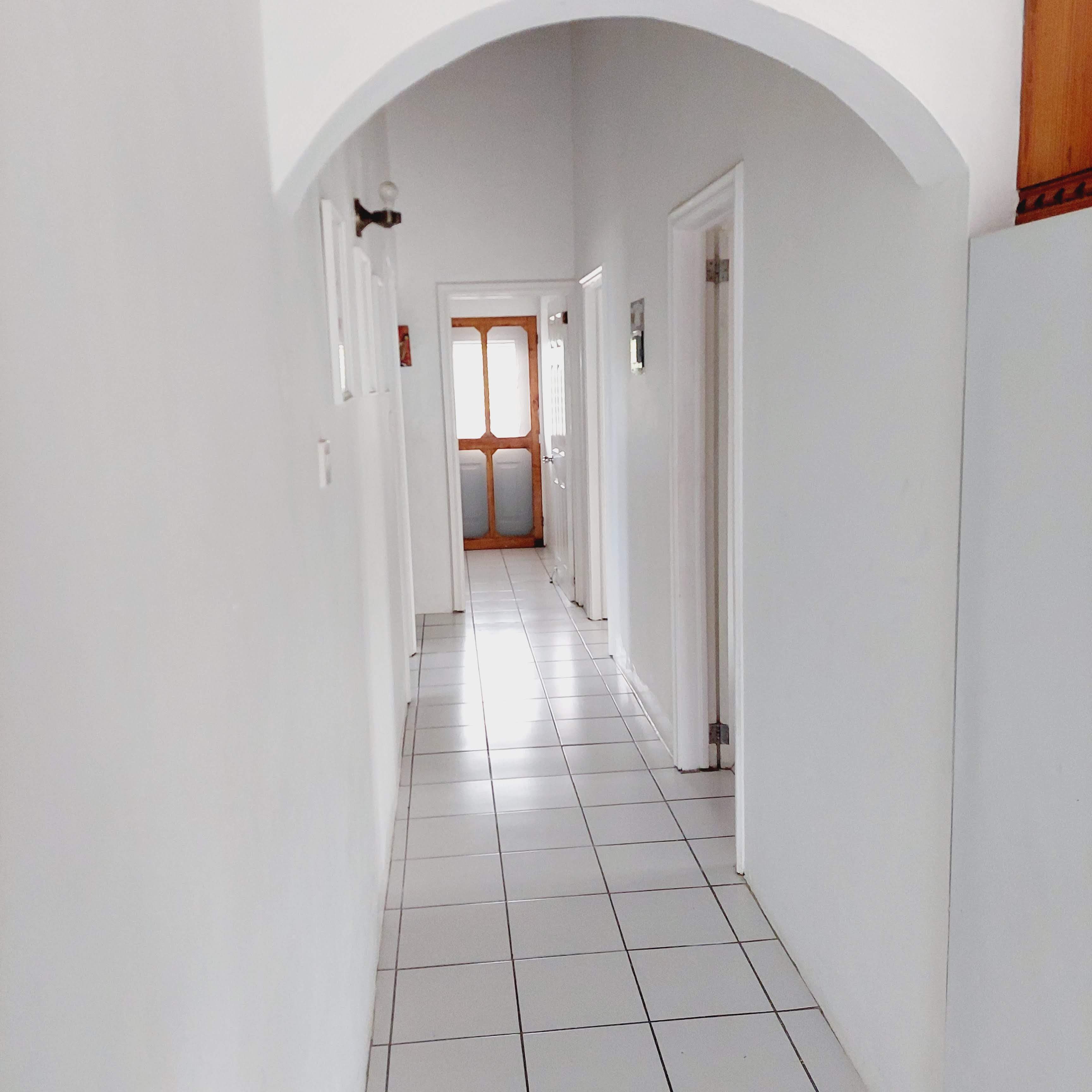Un pasillo con paredes blancas y suelo de baldosas, que conduce a una puerta con marco de madera.
