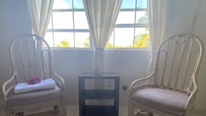 Dos sillones blancos de mimbre con cojines, una mesita y una ventana con cortinas.