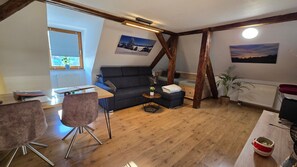 A modern living room with a wooden floor, a black sofa, a dining table, and a chair. - FEWO Gipfelstürmer with Königscard (Nesselwang)