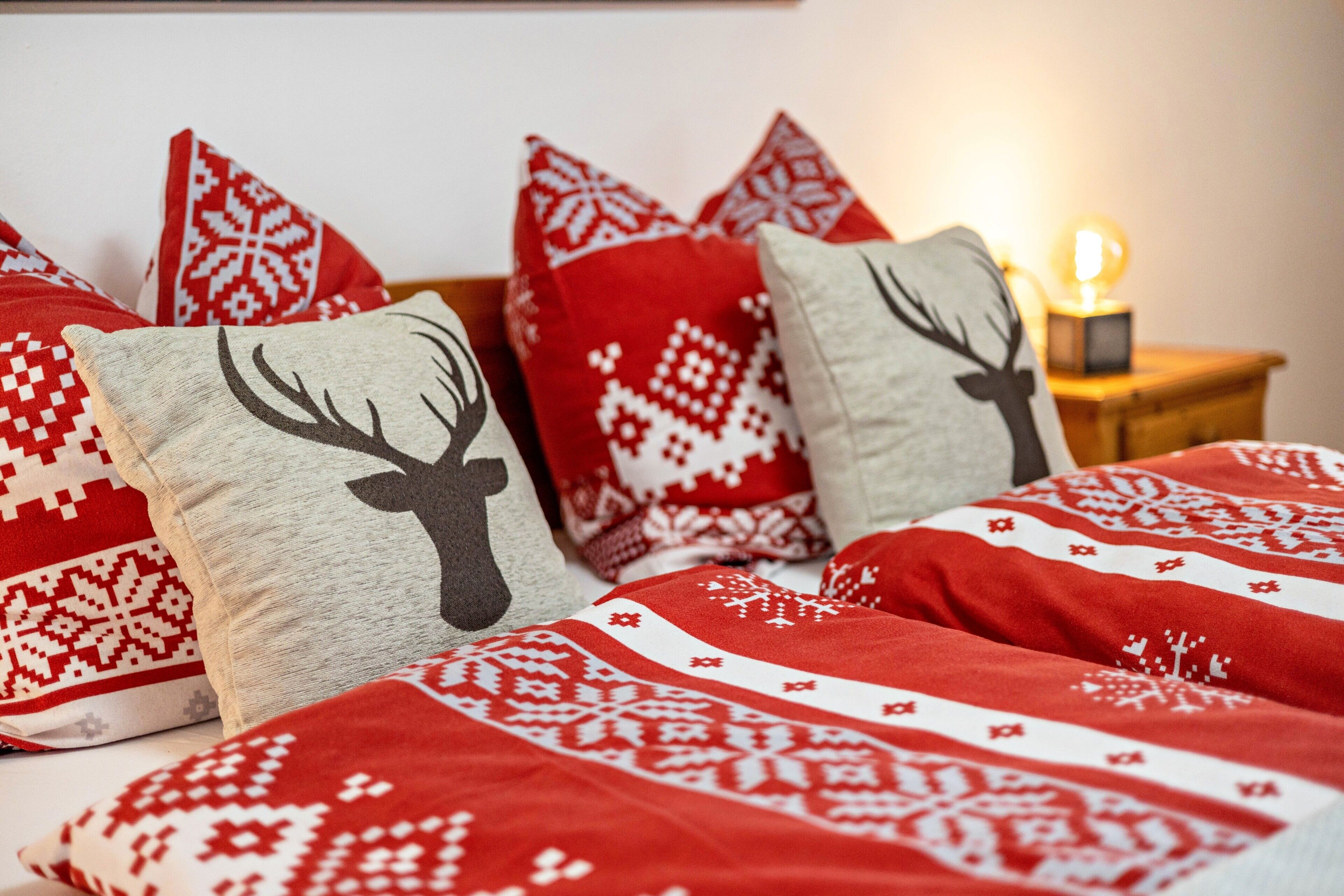 A bed with red and white patterned bedding, a lamp on a bedside table, and a wall with a light switch.
