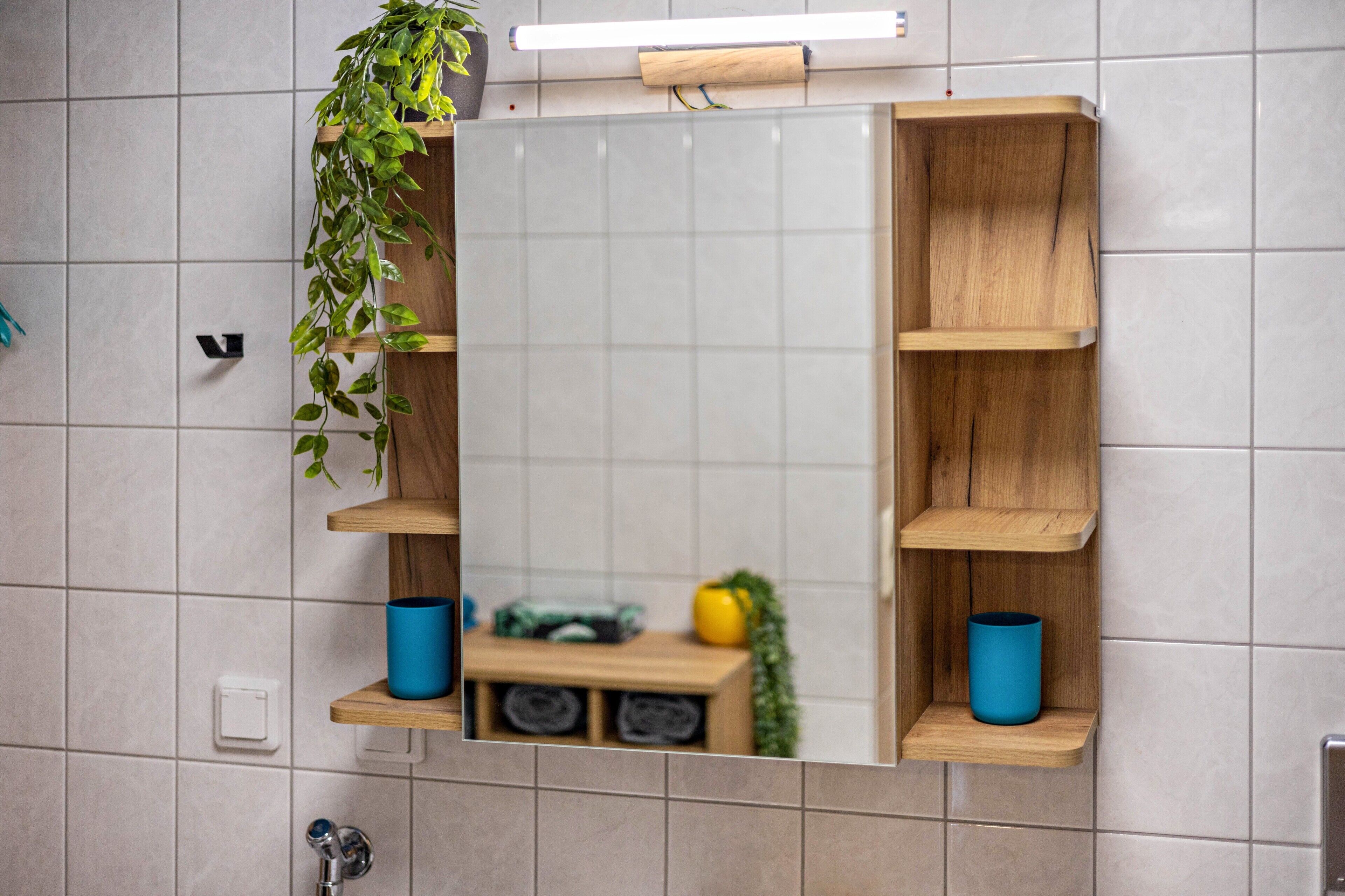 Un baño con espejo, estantes de madera y una planta en maceta.