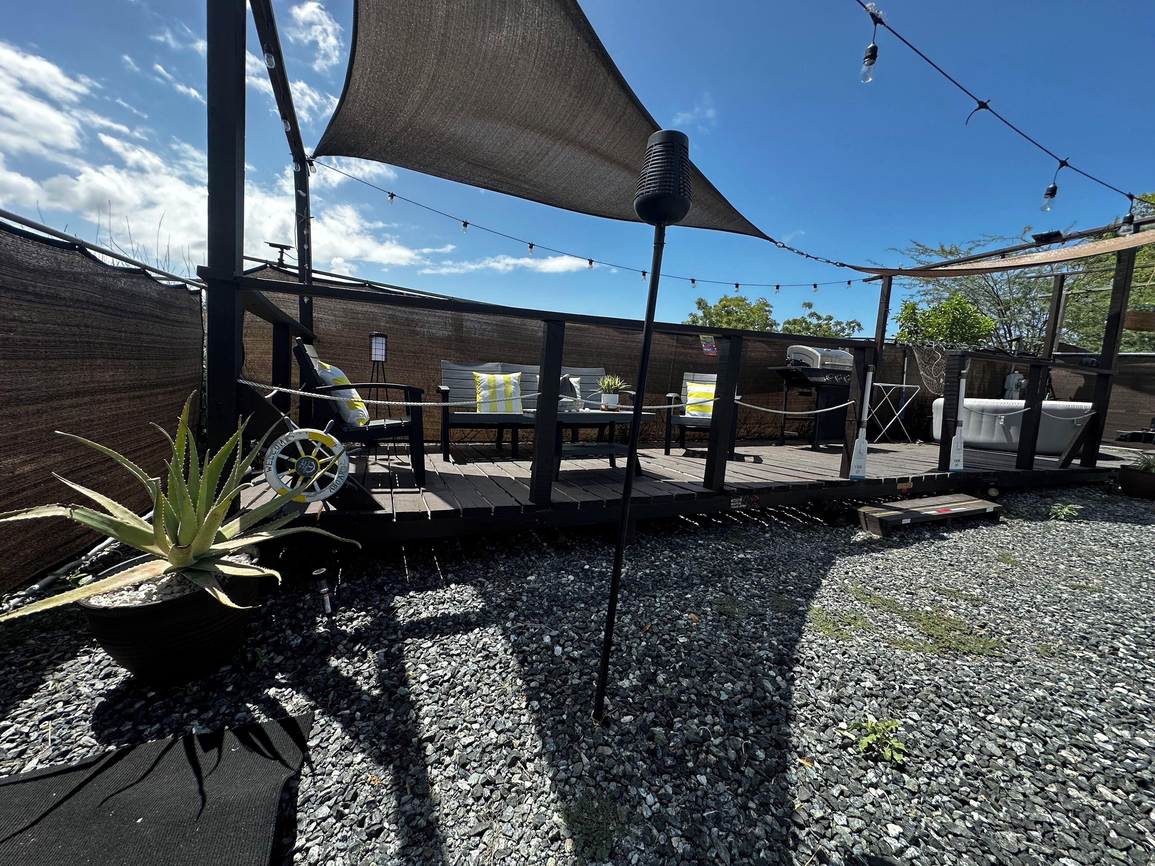 Un patio con mobiliario exterior, una parrilla y una sombrilla grande que da sombra.