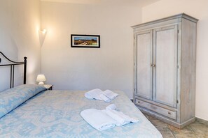 Un dormitorio con cama, mesita de noche con lámpara, armario y un cuadro en la pared.