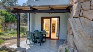 Katettu terassi, jossa on pöytä ja tuoleja, kiviseinä ja ovi, joka johtaa sisätiloihin.