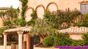 A building with a covered entrance, arched windows, and lush greenery. - Baia Delle Palme Bilocale Premium, Pula ( IT ), Italy (Pula ( IT ))