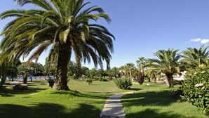 A well-maintained garden with palm trees, a clear pathway, and a pool area in the background. - Baia Delle Palme Bilo Premium, Pula ( IT ), Italy (Pula ( IT ))