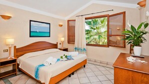 A hotel room with a bed, two bedside tables, a desk, a potted plant, and a window with curtains. - Baia Delle Palme Bilo Premium, Pula ( IT ), Italy (Pula ( IT ))