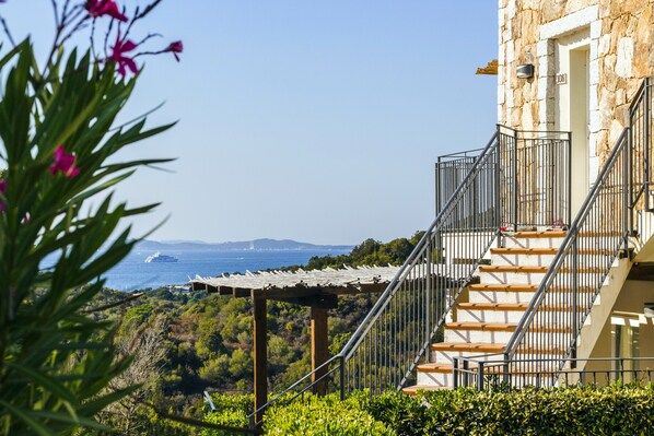 A stone building with a wooden staircase and a pergola overlooking a coastal landscape.