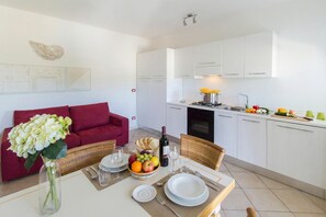 A modern kitchen with white cabinets, a dining area with a table set for two, and a red sofa in the living area. - Ea Bianca Trilocale 2Km From The Beach, Baja Sardinia, Italy (Baja Sardinia)
