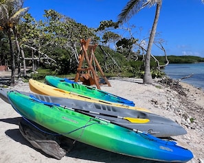 Kayaks alineados en una playa arenosa con una estructura de madera al fondo.