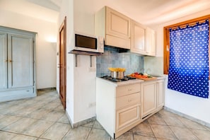 Una cocina con armarios blancos, microondas, estufa y cortina azul con lunares blancos.
