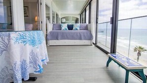 Un balcón con una cama, una mesa y vista al océano.