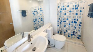 Un baño moderno con lavamanos, inodoro y cortina de ducha blancos, con estampado de lunares azules y blancos.