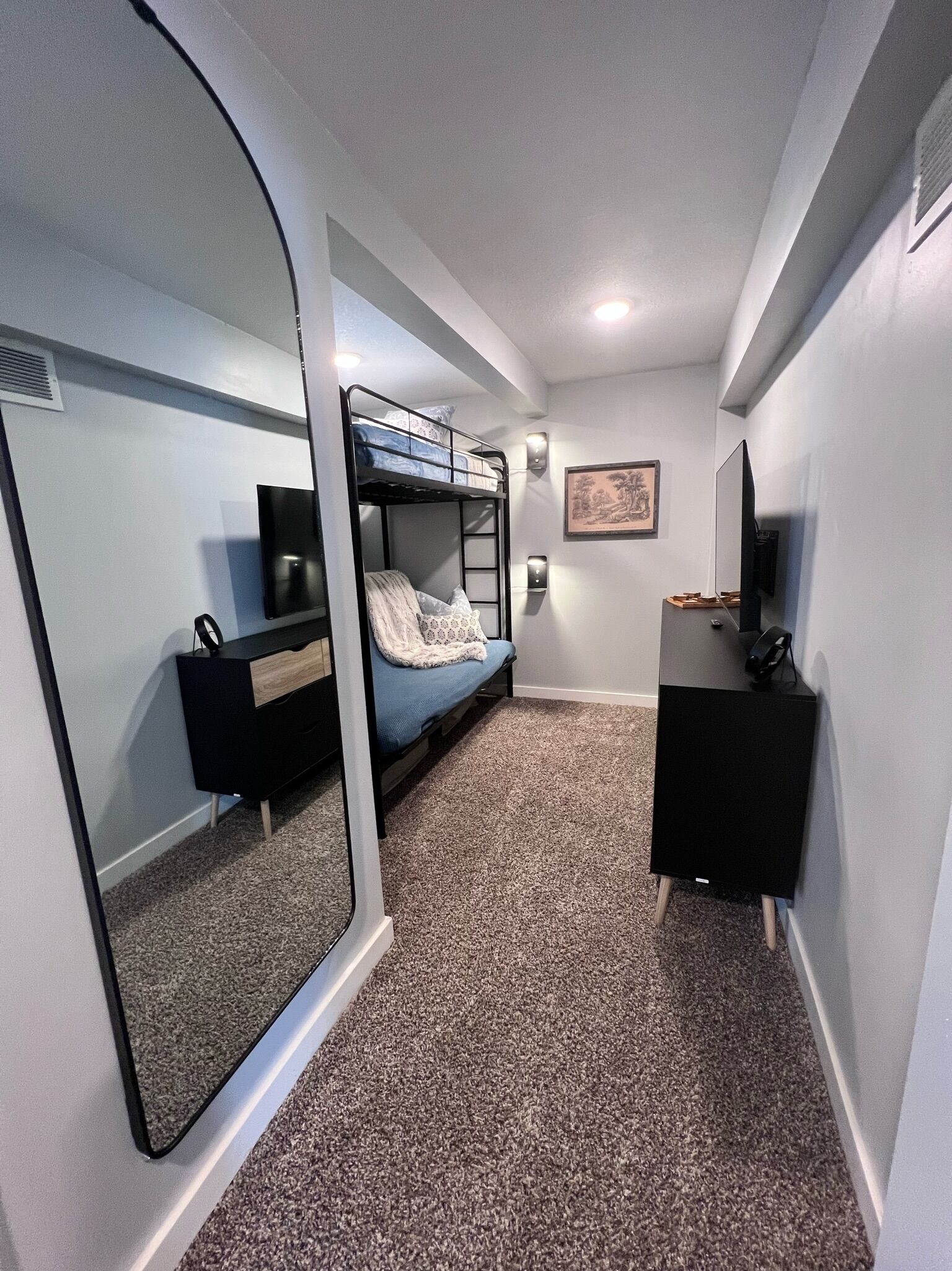 A compact room with a bunk bed, a desk with a computer, a TV, and a large mirror.