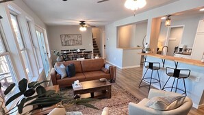 A spacious living area with a brown sofa, a gray armchair, and a coffee table. There is a dining area with a table and chairs, and a kitchen area with a bar and stools. - Get Cozee Pequot Lakes, Lakefront on Mayo/Sibley (Pequot Lakes)