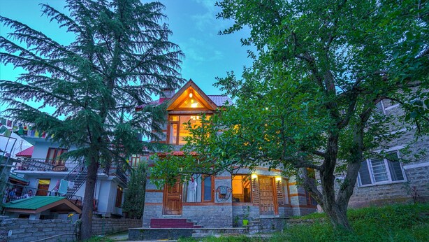 Une maison en pierre à deux étages, dotée d’un balcon en bois, d’un toit rouge et d’une entrée éclairée.