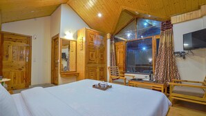 Une chambre à coucher aux murs lambrissés, avec un grand lit, une chaise, un téléviseur et une fenêtre avec des rideaux.