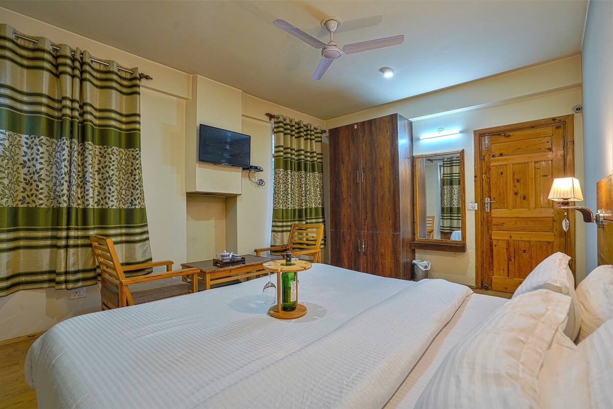 A hotel room with a bed, a desk, a chair, a television, a wardrobe, and a ceiling fan.