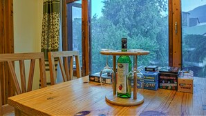 Une table en bois, une bouteille de cidre de pomme, un présentoir en bois et une fenêtre donnant sur des arbres et des bâtiments.