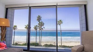 Ein Zimmer mit großem Fenster mit Blick auf einen Strand, Palmen und das Meer.