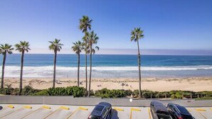 Ein Parkplatz mit Autos und Blick auf den Strand, Palmen und das Meer.