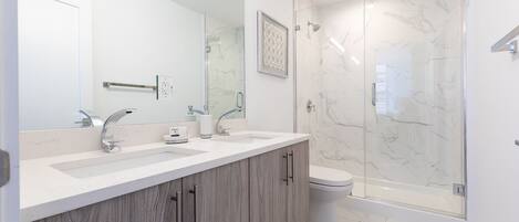 A modern bathroom with a double sink vanity, a glass shower enclosure, and a toilet.