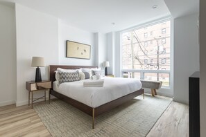 Relax in a serene bedroom with a large bed, bedside tables, and a window offering a city view.