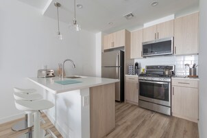 A modern kitchen with a central island, stainless steel appliances, and light wood cabinetry.