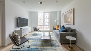 A modern living room with a sofa, a coffee table, a TV, and a large window.