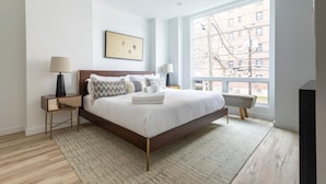 A modern bedroom with a large bed, a view of the city, and a minimalist design.