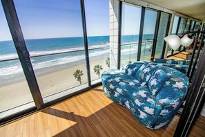 A modern room with large windows overlooking a beach, featuring a wooden floor and a blue floral sofa.
