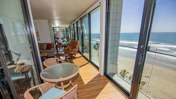 A balcony with a view of the beach, furnished with wicker chairs and a table.