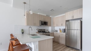 A modern kitchen with wooden cabinets, a stainless steel refrigerator, a microwave, and a stove. - Sun-drenched 3BR Loft With Outdoor Space Near NYC (Hoboken)