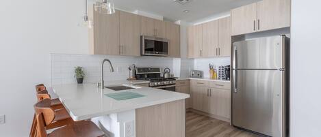 A modern kitchen with wooden cabinets, a stainless steel refrigerator, a microwave, and a stove.