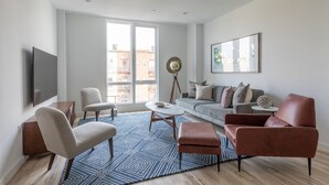A modern living room with a sofa, armchairs, a coffee table, and a television. - Sun-drenched 3BR Loft With Outdoor Space Near NYC (Hoboken)