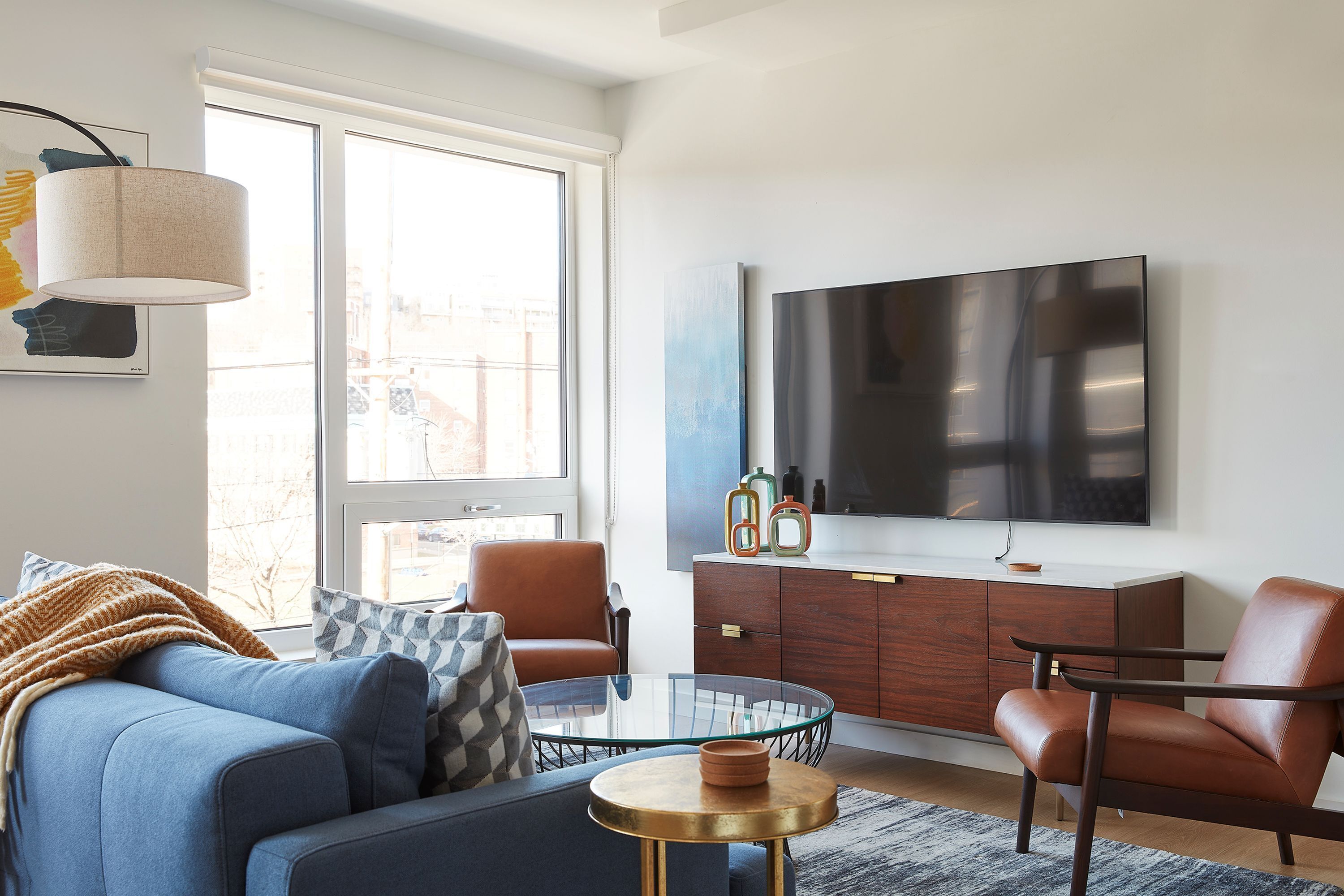 A modern living room with a sofa, armchairs, a glass coffee table, a TV, and a wooden cabinet.