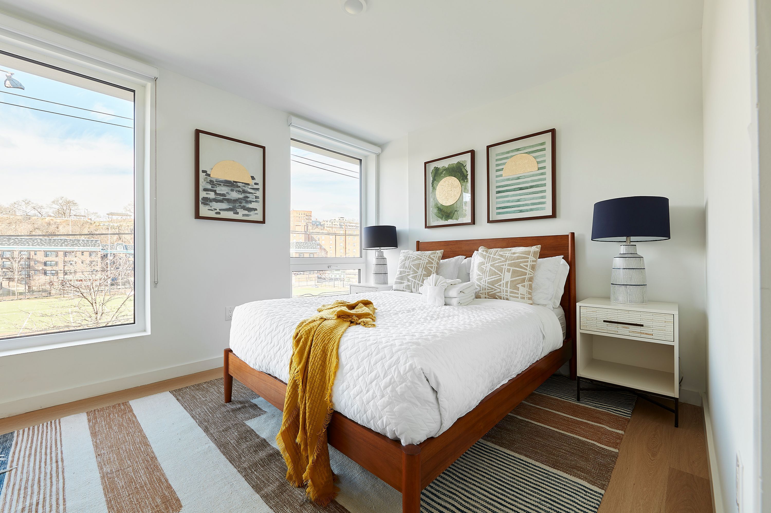 A modern bedroom with a large bed, a nightstand, a lamp, and framed artwork on the walls.