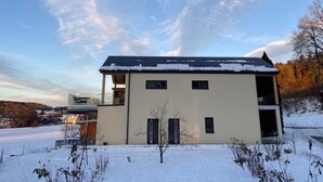 Un bâtiment à deux étages, doté d’un toit plat, d’un balcon à l’étage supérieur et d’un sol recouvert de neige.