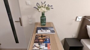 Une pièce comprenant une table en bois sur laquelle sont disposés des magazines de voyage, un vase avec des fleurs et un lit avec un oreiller.
