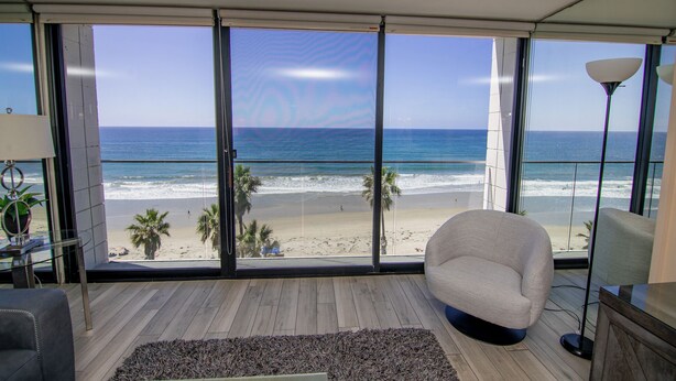 A room with a large window overlooking a beach, a modern chair, and a lamp. - ONE BEDROOM CONDO 609 (San Diego)