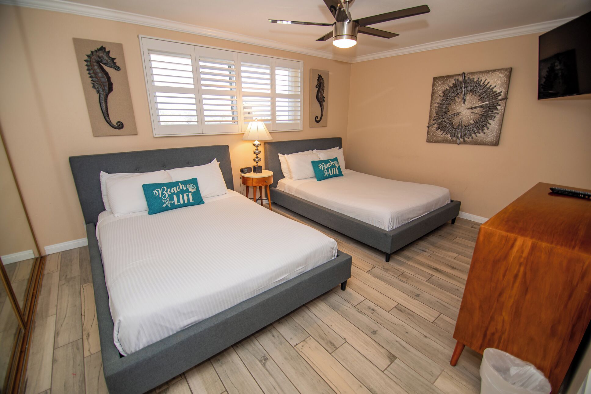 A hotel room with two beds, a ceiling fan, a TV, and a wooden table.