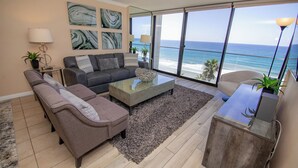A modern living room with a large window overlooking the ocean, a grey sofa, a coffee table, and a small side table with a lamp. - ONE BEDROOM CONDO 609 (San Diego)