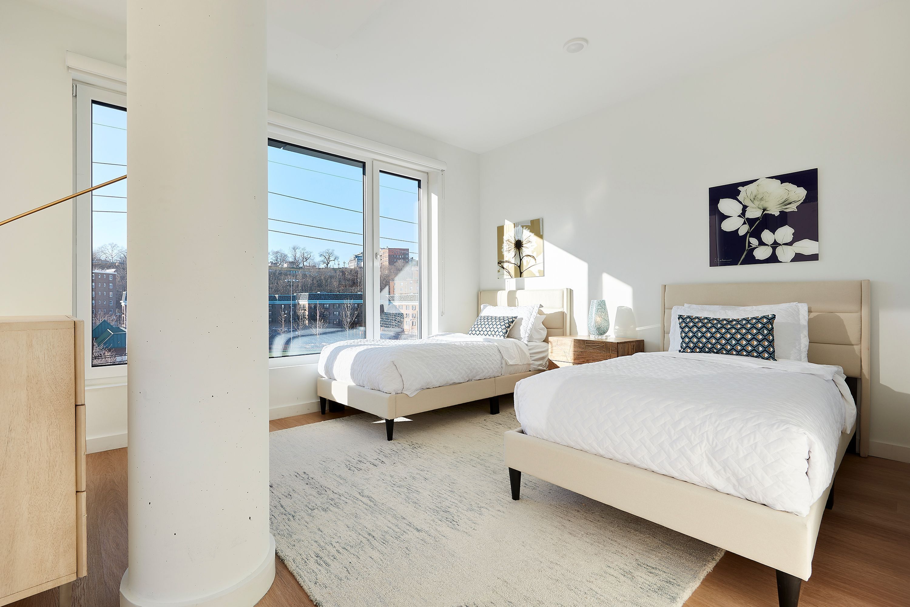A bedroom with two beds, a large window, and a view of the city.