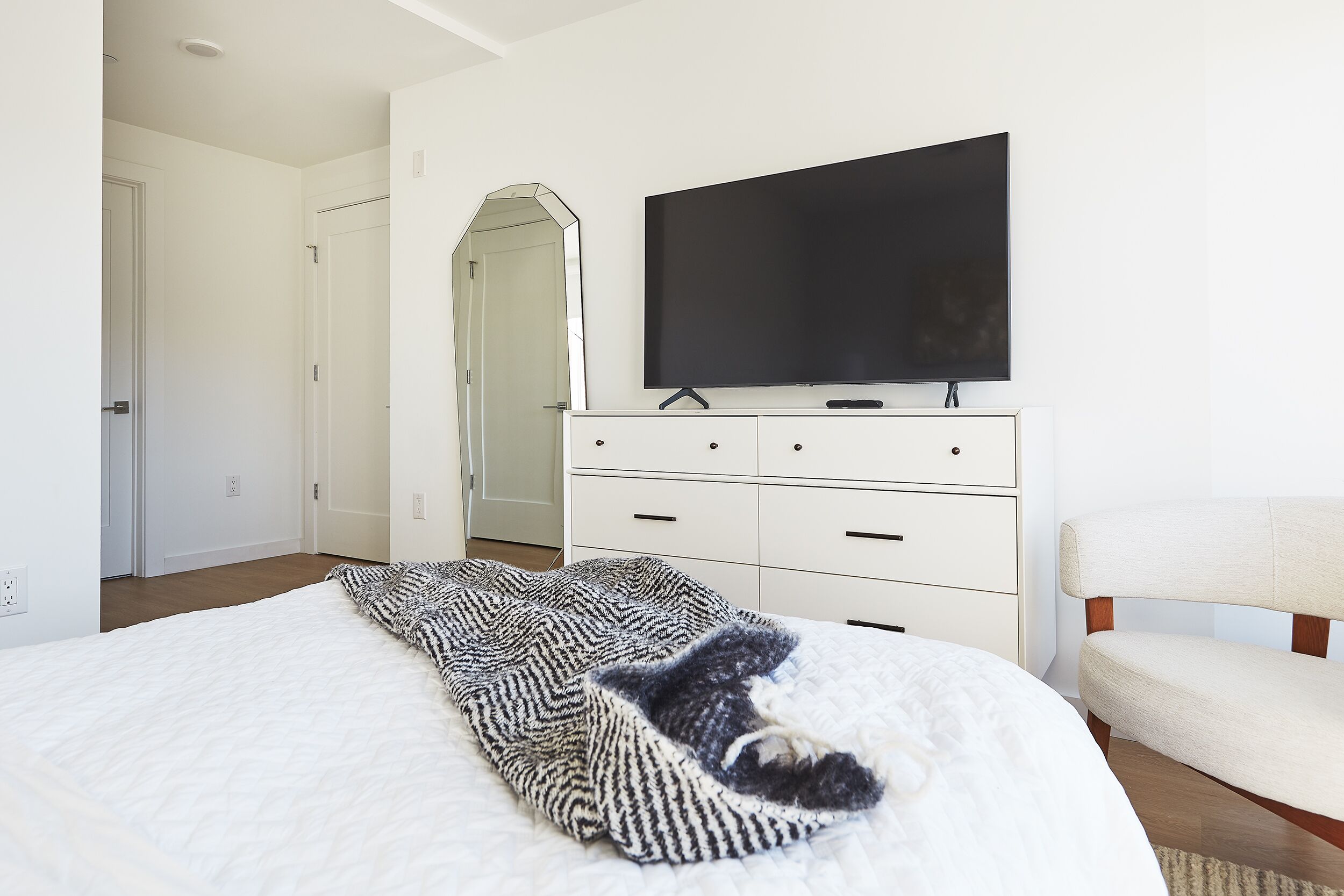 A bedroom with a bed, a television on a dresser, a chair, and a mirror.