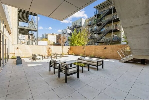 Un patio exterior con mobiliario, una escalera y vistas a edificios cercanos.
