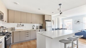 A modern kitchen with a central island, stainless steel appliances, and a dining area with bar stools. - Modern 3 BR Loft -shared Deck - gym - Mins to NYC (Hoboken)