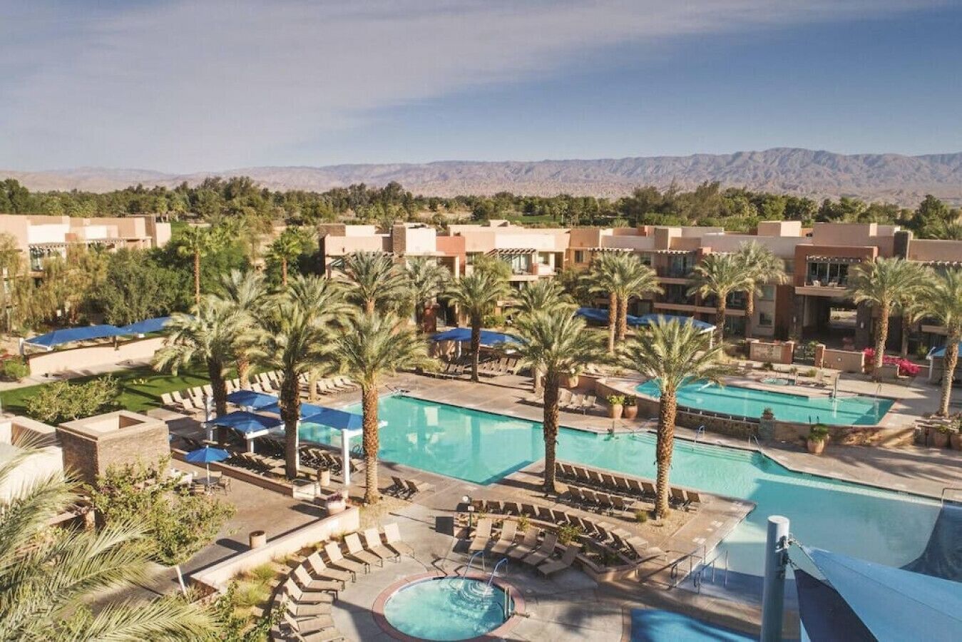 A resort with multiple swimming pools, palm trees, and a mountainous backdrop.