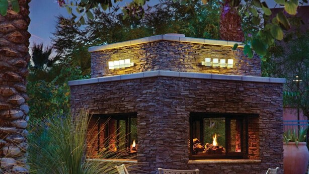 A stone fireplace with two chairs and a table in front, surrounded by plants. - Marriott's Shadow Ridge II (Palm Desert)
