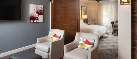 A hotel room with two armchairs, a sofa, a TV, and a bed.