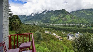 Ein Balkon mit roten Geländern mit Blick auf ein Tal mit Gebäuden und üppigem Grün.